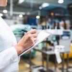 Young happy female worker in factory checking water bottles or gallons before shipment. Inspection quality control.