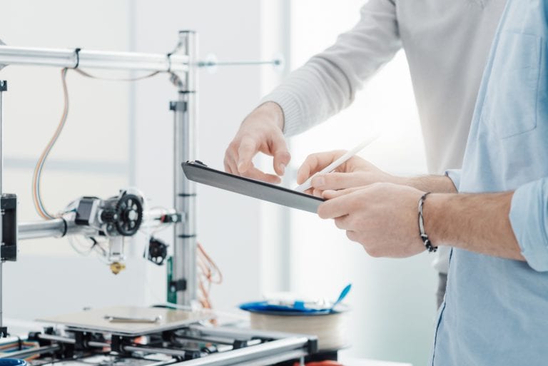 Mechanical engineers in the laboratory using a 3D printer for testing and prototyping, the are checking a list on a clipboard