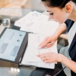 business analyst studying report papers with graphic results of company activity. information processing and data analysis concept. young professional woman at work