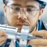 Close-up Shot of the Industrial Engineer Wearing Classes and Hard Hat Connects Two Components He Designed. Precision in Mechanical Engineering.