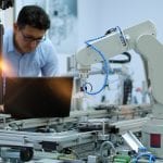 Industry 4.0 workshop in an automation education center. Engineer is programming PLC. Focus on Gripper which picks up the product from an automated car and programming engineer at the background.